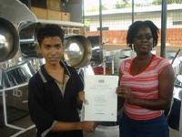 Jonathan Chang being presented his certificate with distinction, by steelpan tutor Adelle Joseph of birdsong Steel Orchestra