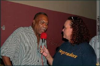 Wearing her Desperadoes 'T-Shirt', Allison Hennessy interviews Len "Boogsie" Sharpe at the 'wake' for the late Clive Bradley in Desperadoes' Panyard