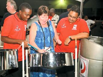 Canadian freelance journalist Theresa Storm plays the steelpan under the watchful eyes of her Phase II Pan Groove tutors Rondell Williams, left, and Ronald Mohammed